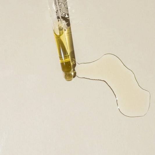 Pipette déposant une huile dorée sur fond beige, texture sérum huileux pour routine visage au bakuchiol.