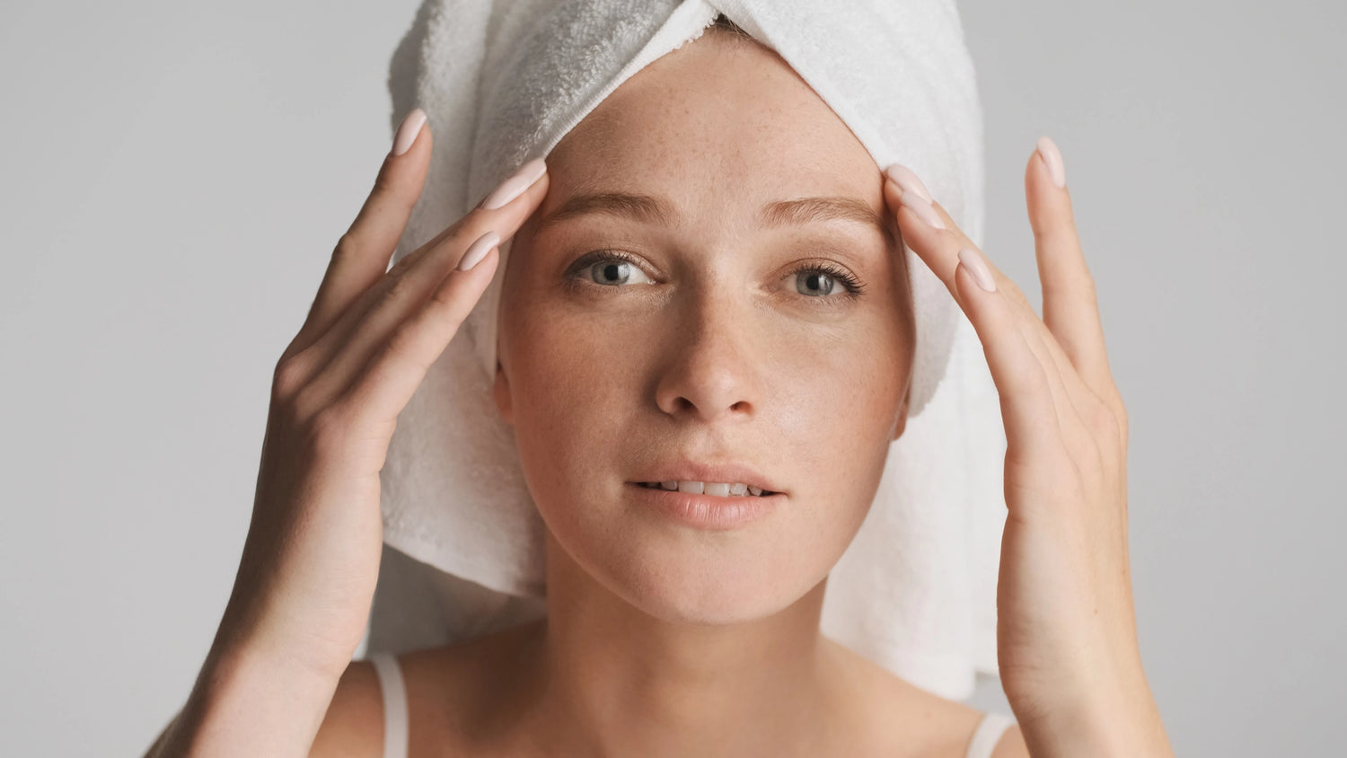 Femme avec serviette sur la tête massant le visage, routine soin douce peau sensible (bakuchiol).
