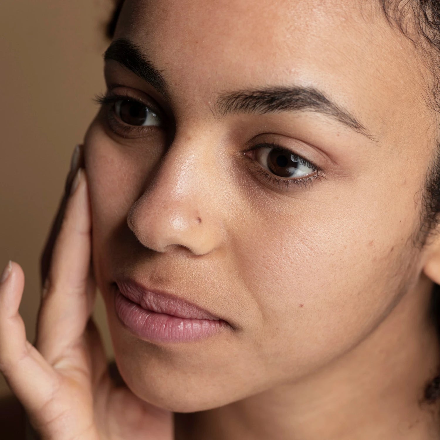 Gros plan visage peau naturelle, main sur la joue, illustration d’un soin visage doux au bakuchiol (alternative au rétinol).
