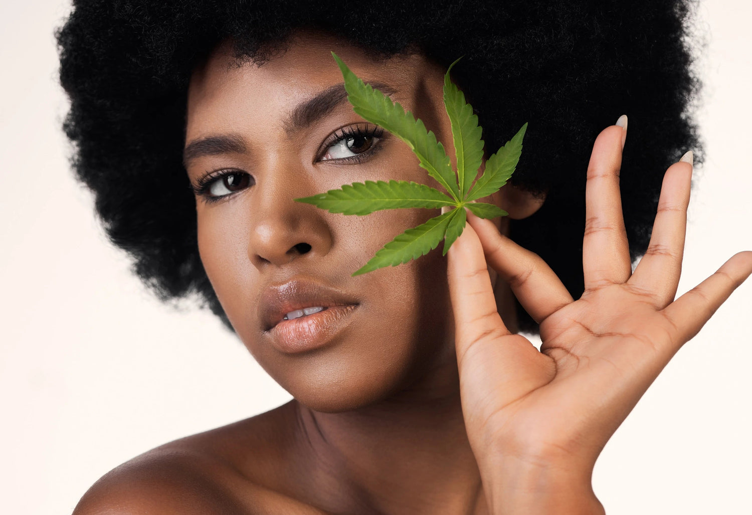 Femme tenant une feuille de chanvre devant le visage, visuel pour article sur le CBD en cosmétique