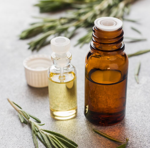 Flacons d’huiles essentielles sur surface neutre avec brins de romarin, illustration pour article sur parfum, huiles essentielles et allergènes en cosmétique.