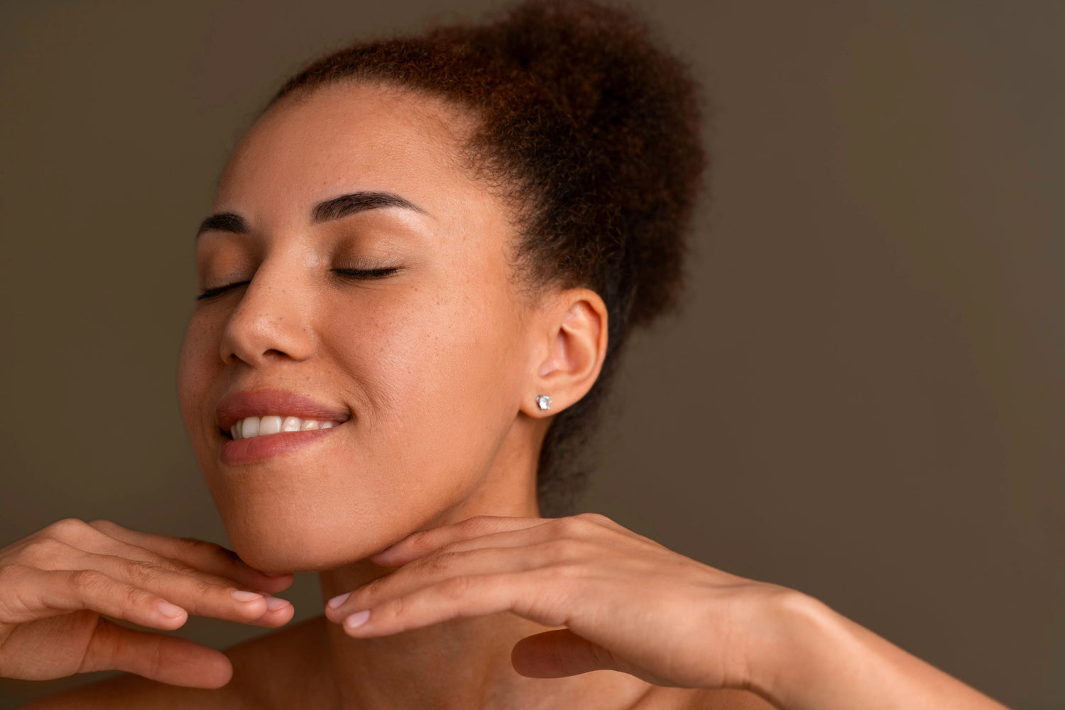 Femme souriante aux yeux fermés, mains sous le menton, peau nue lumineuse, visuel routine soin visage Seomse pour un teint plus frais.