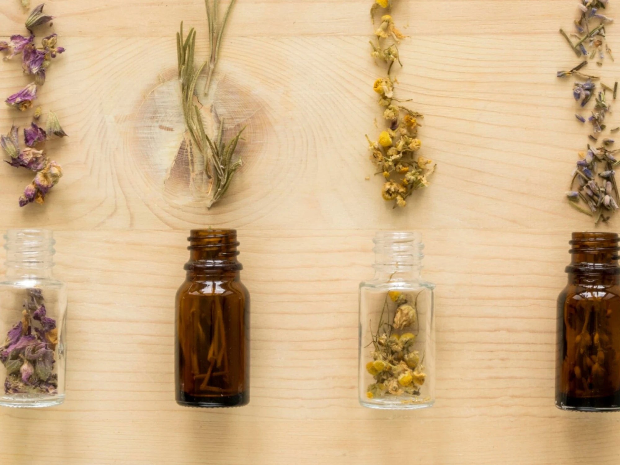 Flacons en verre et plantes séchées sur fond bois, visuel parfum, huiles essentielles et allergènes en cosmétique.