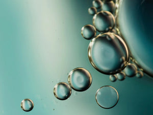 Bulles dans une texture aqueuse, illustration acide hyaluronique et hydratation de la peau.