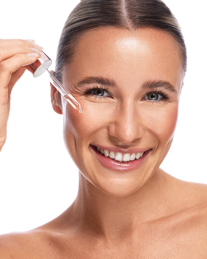 Femme avec une pipette de sérum visage, goutte de soin avant application, routine skincare sur fond blanc.